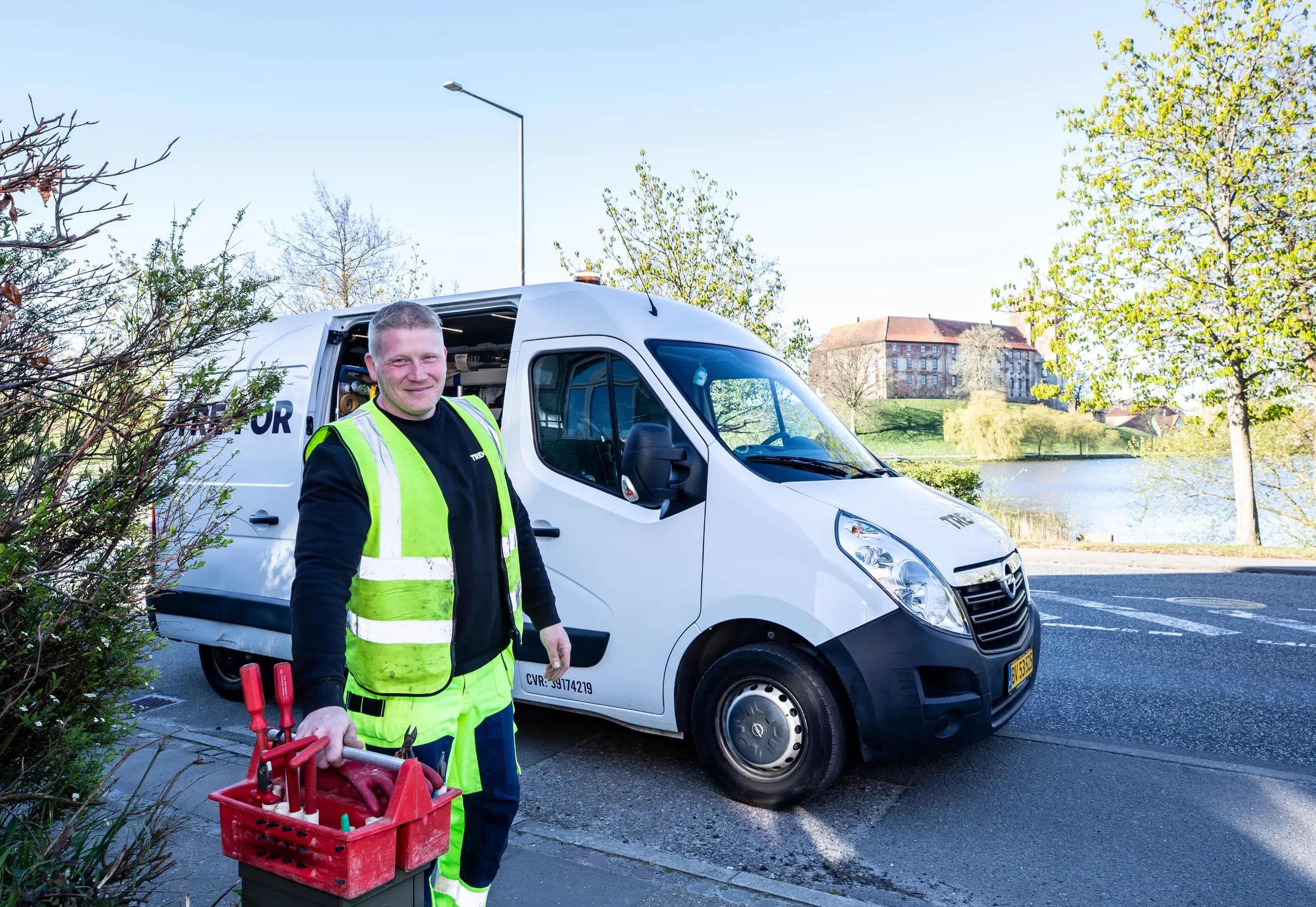 Monteur in werkkleding met zijn gereedschapskist naast een witte bedrijfsbus